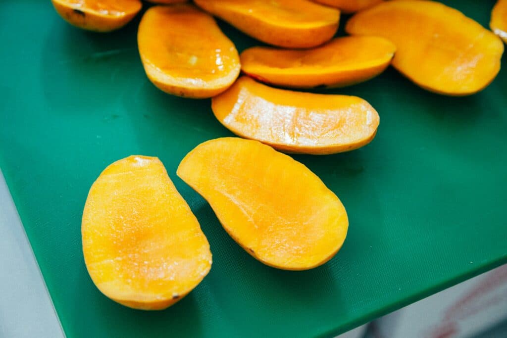 A group of sliced mangoes on a green surface.