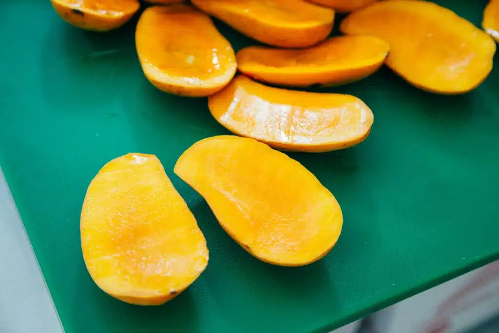 A group of sliced mangoes on a green surface.