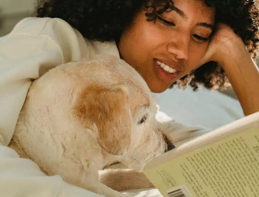 A woman relaxes on her bed on a sunny afternoon while reading her favourite book with her trusty pooch by her side