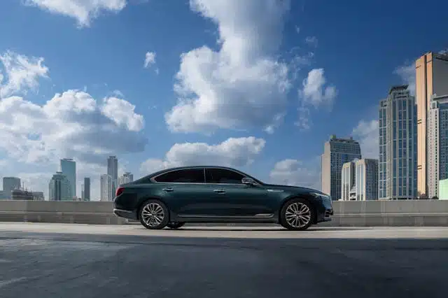 A green hydrogen sedan parked on an urban rooftop parking lot with skyscrapers and a clear blue sky in the background.