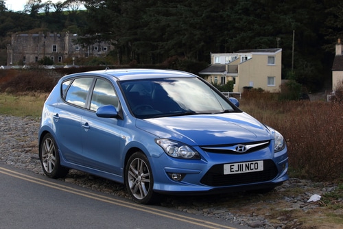 Best used blue Hyundai car parked by the roadside with buildings in the background.