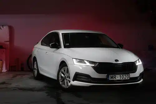 White sedan parked in a dimly lit area with pink ambient lighting.