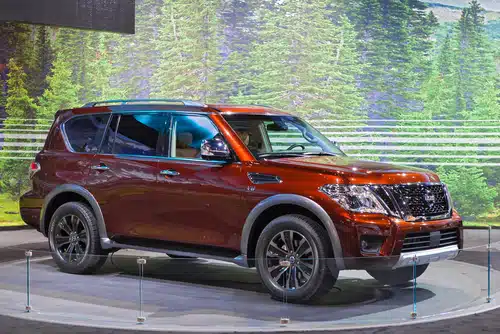 A red SUV on display at an auto show with a forest backdrop, listed among the best second-hand cars in Australia.