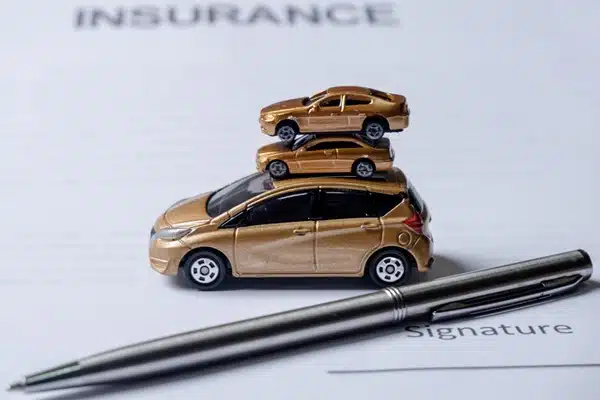 Three miniature cars stacked on top of each other beside a pen on an insurance document with car insurance questions ready for signature.
