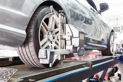 A car elevated on a lift in a garage with an important wheel alignment machine attached to its tire.