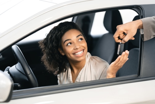 A person seated in a car receives a set of car keys from another individual, signaling the Vehicle Ownership Change.