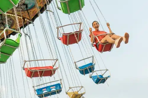 A person in a red dress enjoys a ride on a colorful swing carousel at the Perth Royal Show this year, smiling with arms raised and feet outstretched. The clear sky in the background is just one of the many reasons to attend.