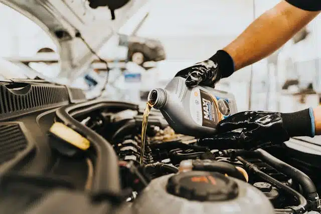 Wearing gloves, the person is pouring motor oil into the car engine, ensuring everything is set for holiday road trip adventures.